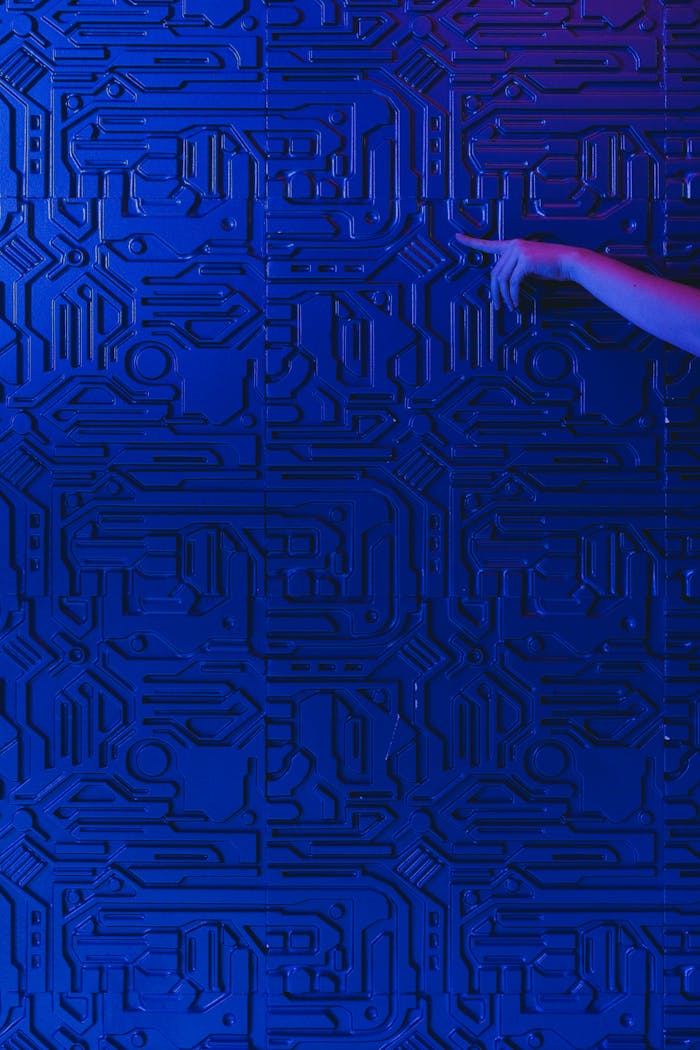A blue circuit board pattern with a human hand pointing, highlighted by blue lighting.